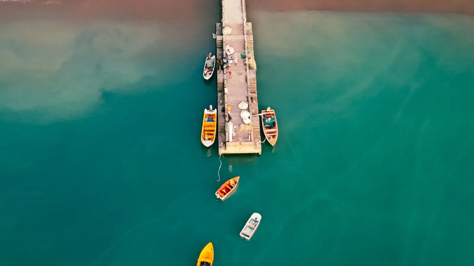Vue aérienne d’un ponton et de barques colorées dans une eau émeraude, lumière dorée