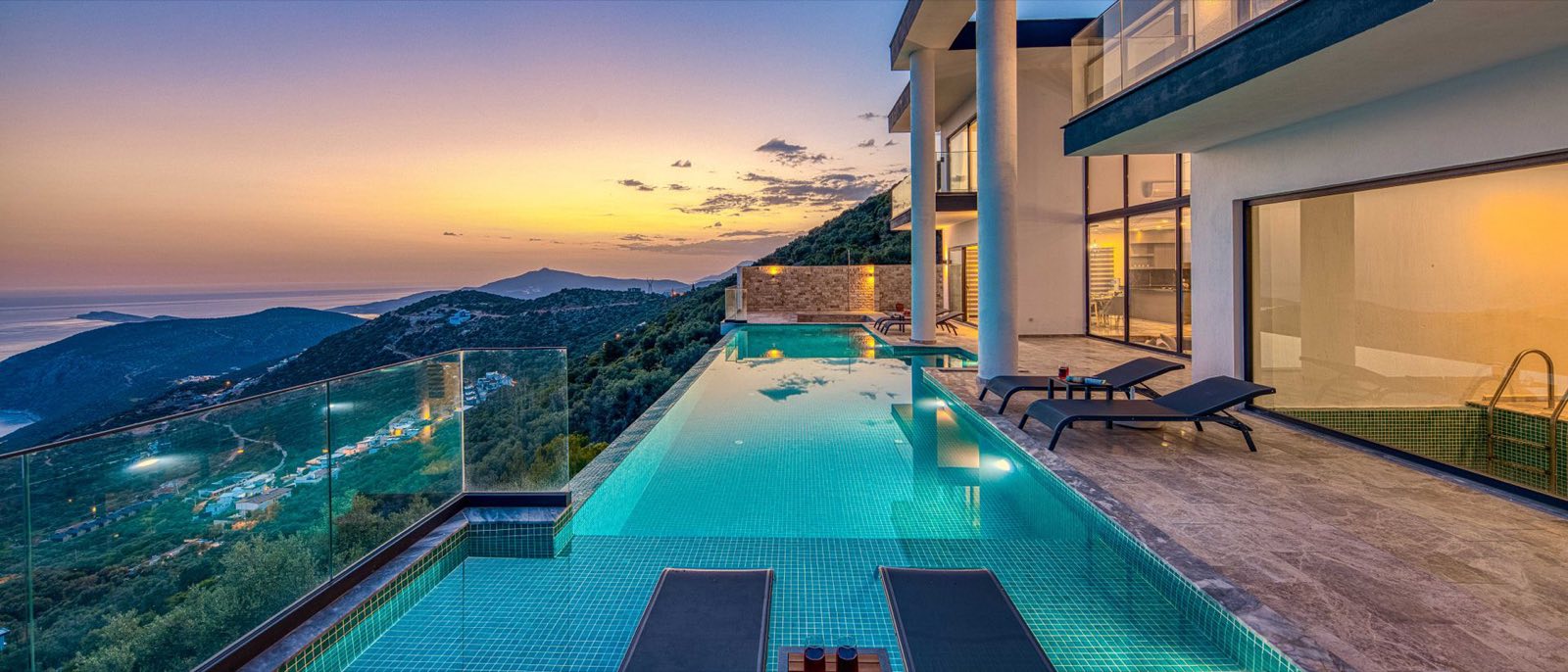 Villa moderne et sa piscine à débordement turquoise face à la mer au coucher du soleil